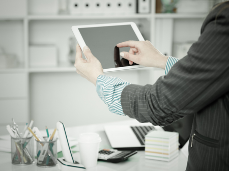 Woman using touchscreen tablet on background with blured office interiorの写真素材