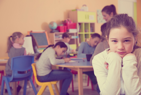 Portrait of sad unhappy schoolgirl and children drawing in classroomの写真素材