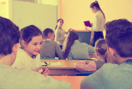 Happy pupils chattering sitting on back desks at lesson in elementary schoolの写真素材
