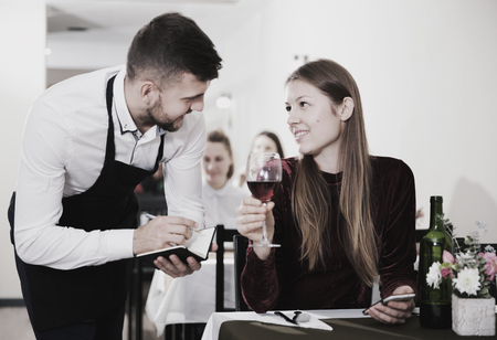 Waiter is taking order from young female in restaurante indoor.の写真素材