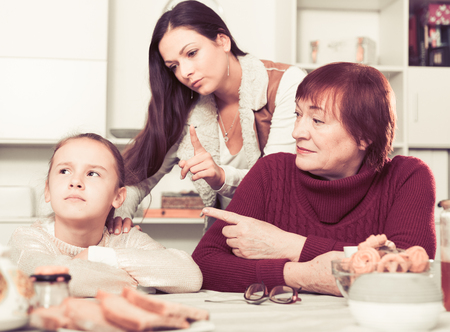 Portrait of upset little girl scolded by mother and grandma at homeの写真素材