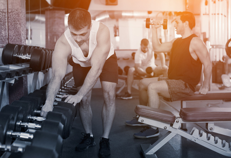 Sporty man choosing dumbbells during weightlifting workout at gymの写真素材
