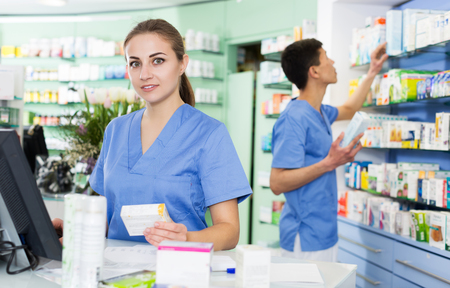 positive female and male specialist are attentively stocktaking medicines with notebook near shelves in pharmacy.の写真素材