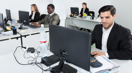 Handsome bearded man confidently working on computer in modern open plan office 