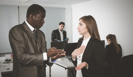 Outraged African American businessman expressing dissatisfaction with work of frustrated girl in coworking spaceの写真素材
