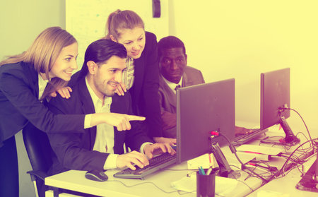 Group of glad young business people grouped around computer monitor, discussing new project in...