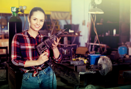 Portrait of young female master standing with drill in workshopの写真素材
