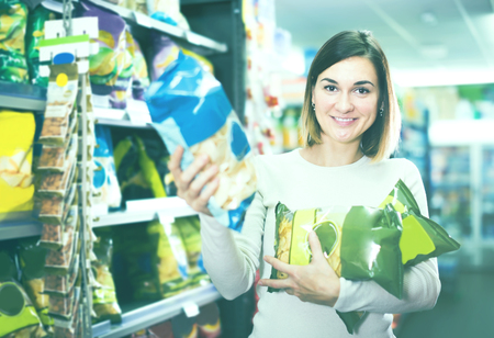 young girl customer looking for tasty snacks from shelves in supermarketの写真素材