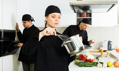 Smiling female kitchener in uniform is standing with pot in the kitchen at the restaurant.の写真素材