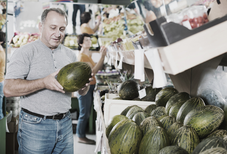 Adult man is choosing ripe melon in the fruit storeの写真素材