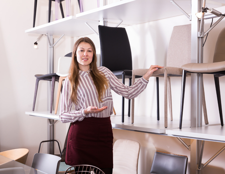 Young attractive saleswoman offering soft modern chair in furniture salonの写真素材