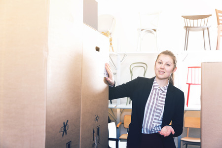 Portrait of successful female owner of chair store standing among cartons with new furniture の写真素材