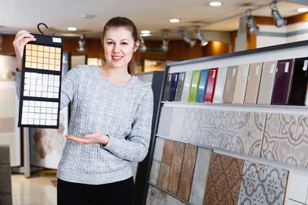 Portrait of glad  positive female looking sample of  ceramic tile  in shopの写真素材