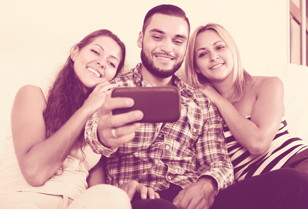 Cheerful young friends making joint portrait using camera in phone at home. Selective focusの写真素材