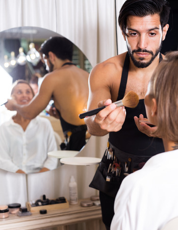 male makeup artist in apron applying cosmetics for female
の写真素材