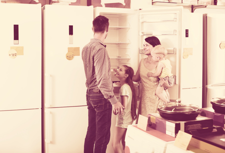 smiling customers with two children choosing new fridge in household storeの写真素材
