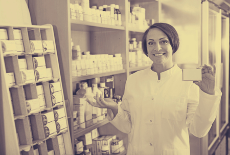 Portrait of positive mature pharmacist woman with biologically active dietary supplement package in storeの写真素材