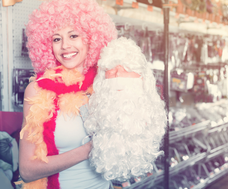 Happy glad  young woman preparing to fest and choosing clown wigの写真素材