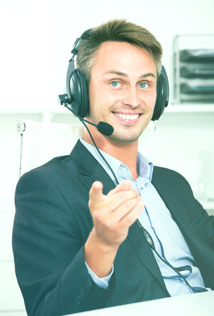 Happy young man talking using hands-free set at customer service officeの写真素材