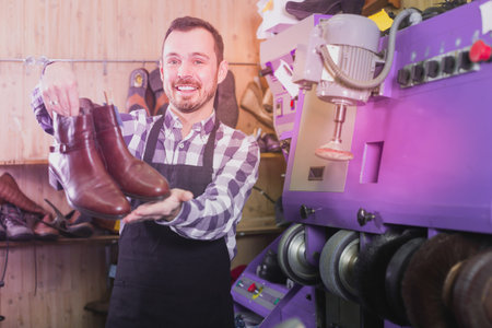 Glad worker displaying result of his work in shoe repair workshop