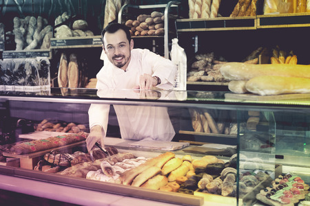 Young seller offering fresh tasty bun in bakeryの写真素材