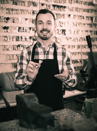 happy male worker showing key he made in repair workshopの写真素材