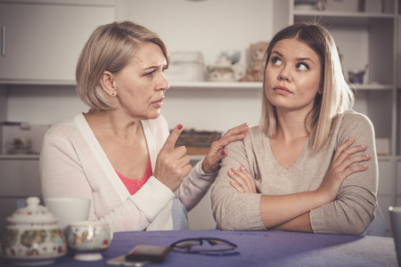 Dissatisfied elderly mother chastises saddened grown-up daughterの写真素材