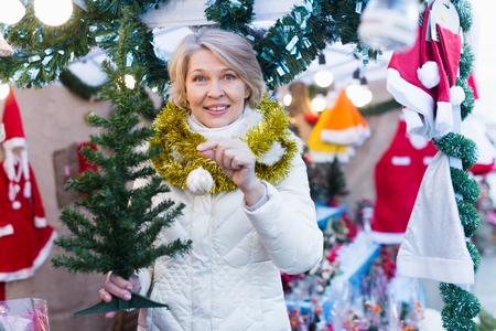 Portrait of mature female in tinsel choosing Christmas tree at fair 

の写真素材