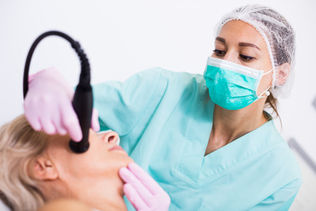 Beautician doing innovative procedure of cryoliposuction to female in cosmetic officeの写真素材