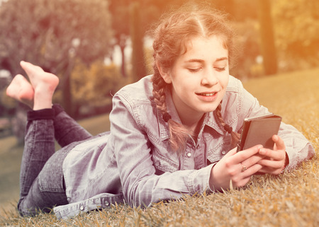 smiling young european girl using digital tablet while lying in green spring  gardenの写真素材