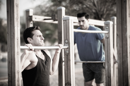 Two friends 30 years old are doing pull-ups for strength in the park near sea.の写真素材