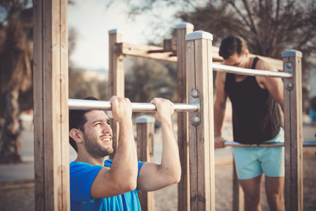 Portrait of sportsmen who are pulling-up in the park near sea.