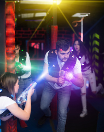 Emotional guy playing laser tag with friends on dark labyrinth in colorful beams of laser pistols の写真素材