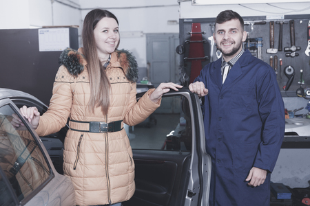 Young woman is satisfied of tire replacement of her car in winter in workshop.の写真素材