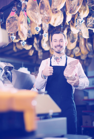 Male shop assistant demonstrating piece of meat in butcherâs shopの写真素材