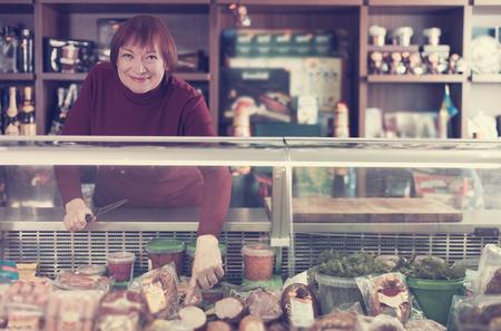 senior  seller woman offering sausage products in the food storeの写真素材