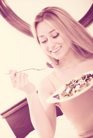 Portrait young blond woman lying in the bed and eating a green saladの写真素材