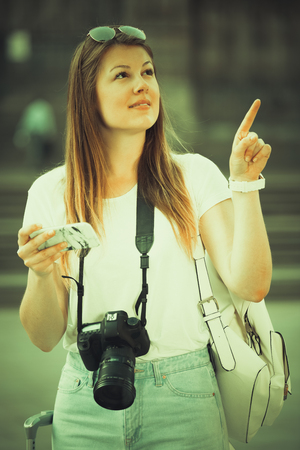 Young cheerful woman having mobile phone in hands and looking for the map in the phoneの写真素材