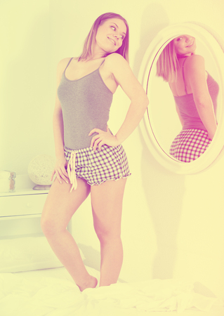 Portrait of girl in pygama looking at mirror in bedroom in morning の写真素材