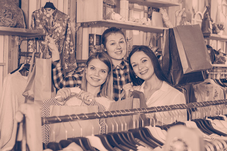 Smiling young women  friends carrying paper bags and clothes  in fashion storeの写真素材