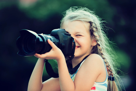 Portrait of cheerful little girl making photo with big professional camera in hands outdoors
の写真素材