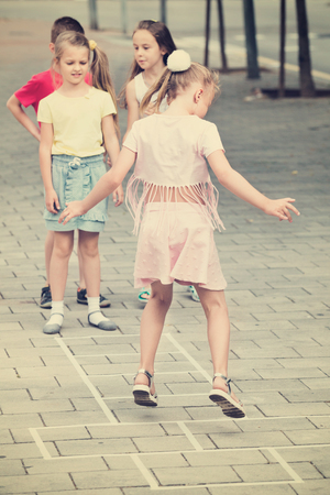 Smiling happy kids in elementary school age playing hopscotch outdoorsの写真素材