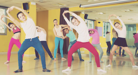 Group of tweens training movements of modern dance in choreography class with woman coach