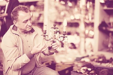  positive man is visiting market of old things and choosing old lamp outdoors.の写真素材