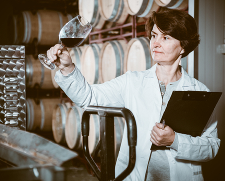 Elderly woman in uniform expertise of red wine on wineryの写真素材