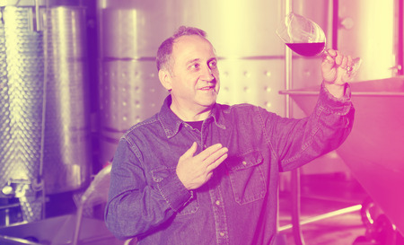 Elderly worker of winery tasting wine  near tanksの写真素材