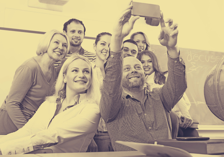 Smiling students posing in a classroom while their lecturer is taking a group selfie with his phoneの写真素材