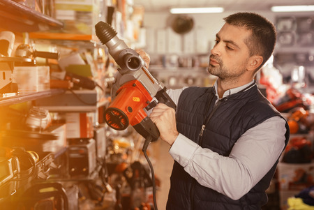 Adult diligent friendly smiling positive  male is standing with puncher in tools store.の写真素材