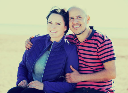 Mature positive couple sitting together on the bench and holding each other