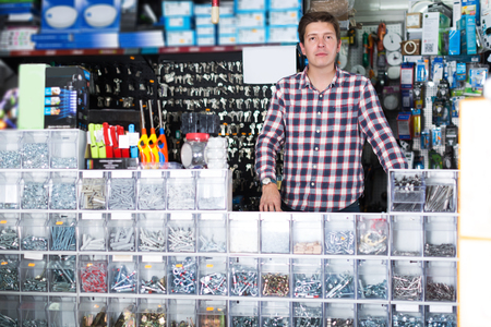Young glad employee selling nuts, screw and fasteners in hardware storeの写真素材